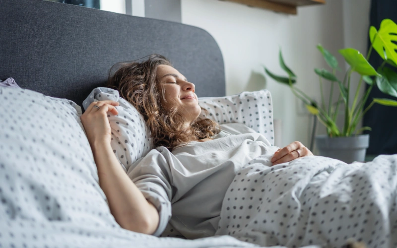 Mujer relajada en la cama disfrutando de un mejor estado de ánimo tras dormir bien