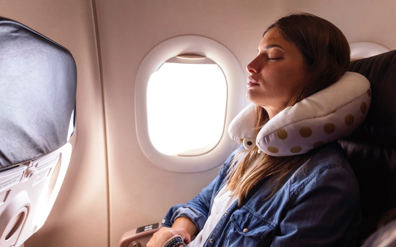 Mujer durmiendo en el avión con una almohada de viaje en forma de U alrededor del cuello