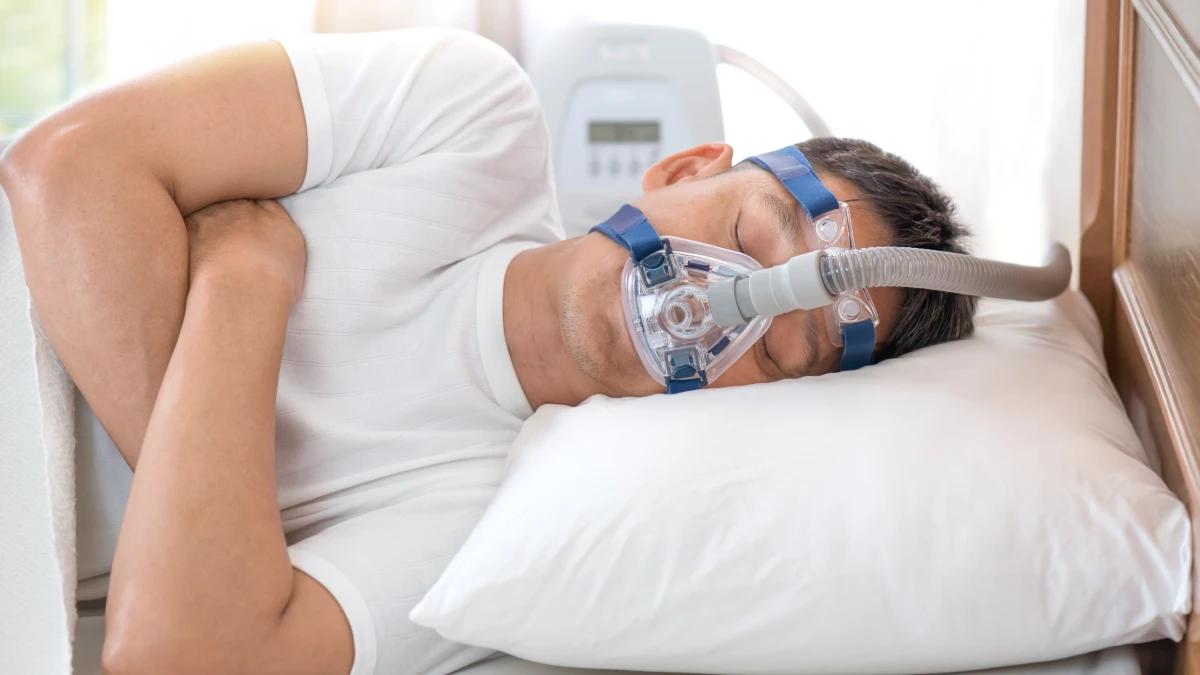 Hombre durmiendo de lado con mascarilla CPAP para la apnea del sueño apoyado en la almohada