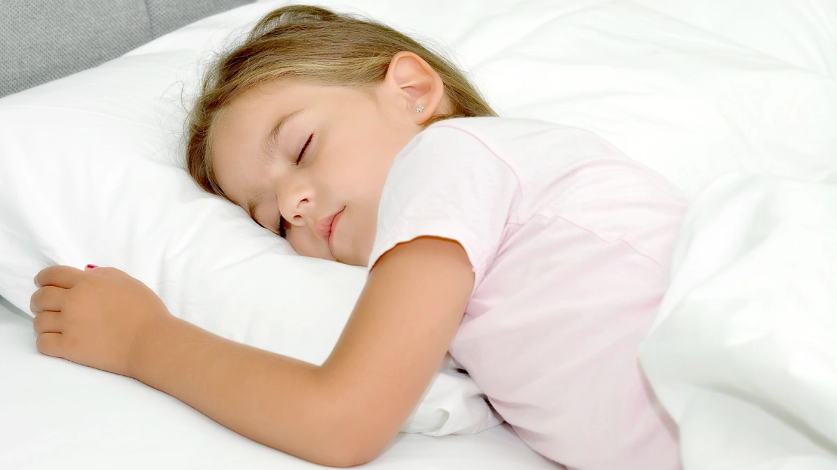 Niña pequeña durmiendo tranquila en su cama con una almohada infantil de altura baja