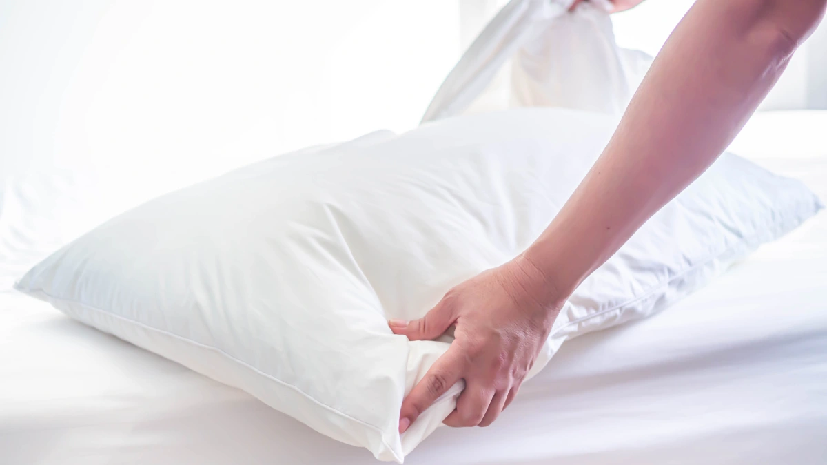Manos colocando una funda de algodón blanca a una almohada sobre la cama